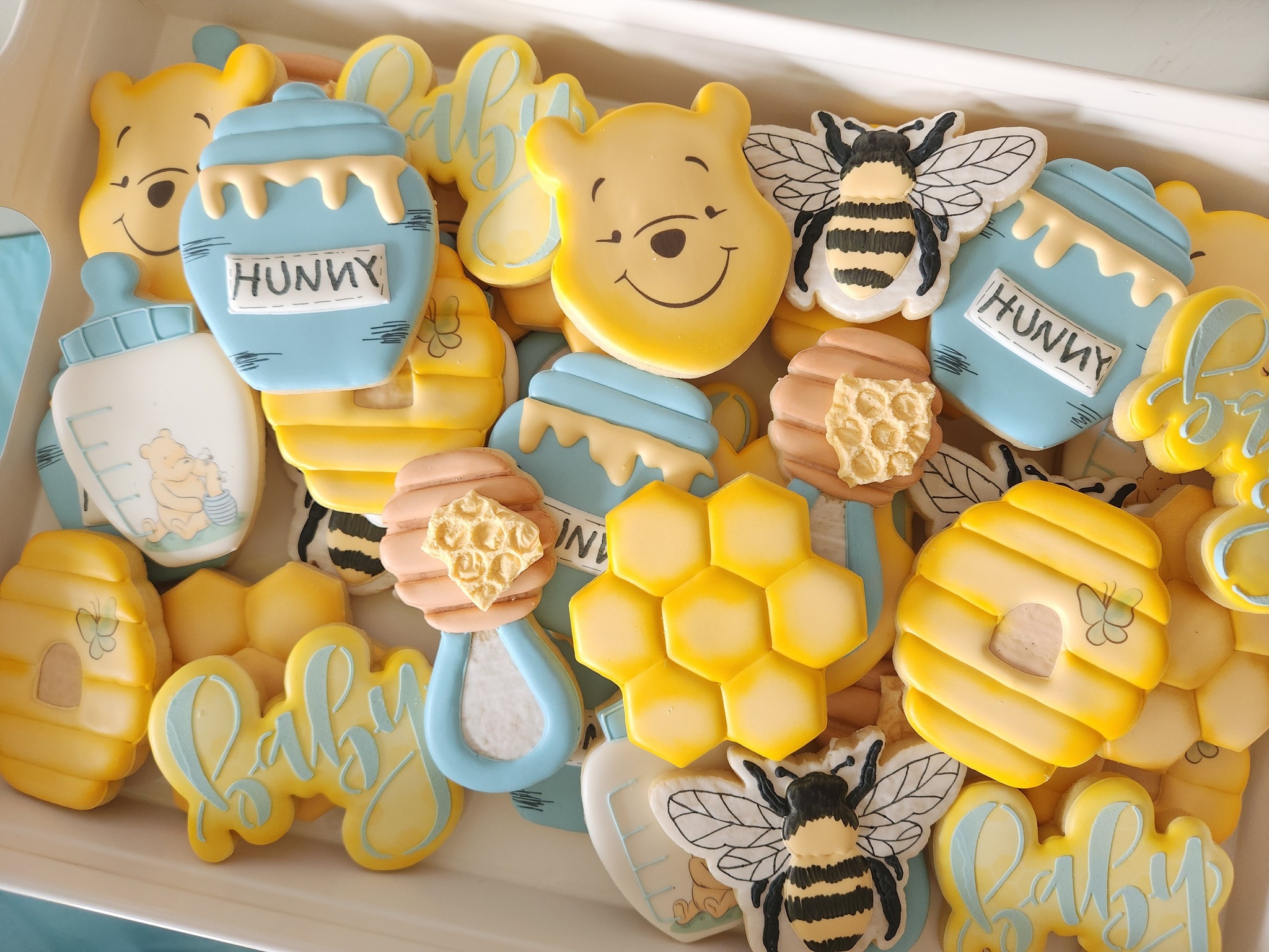 Yellow and blue honey bear baby shower cookies with honey pots, bees, honeycomb, and baby lettering